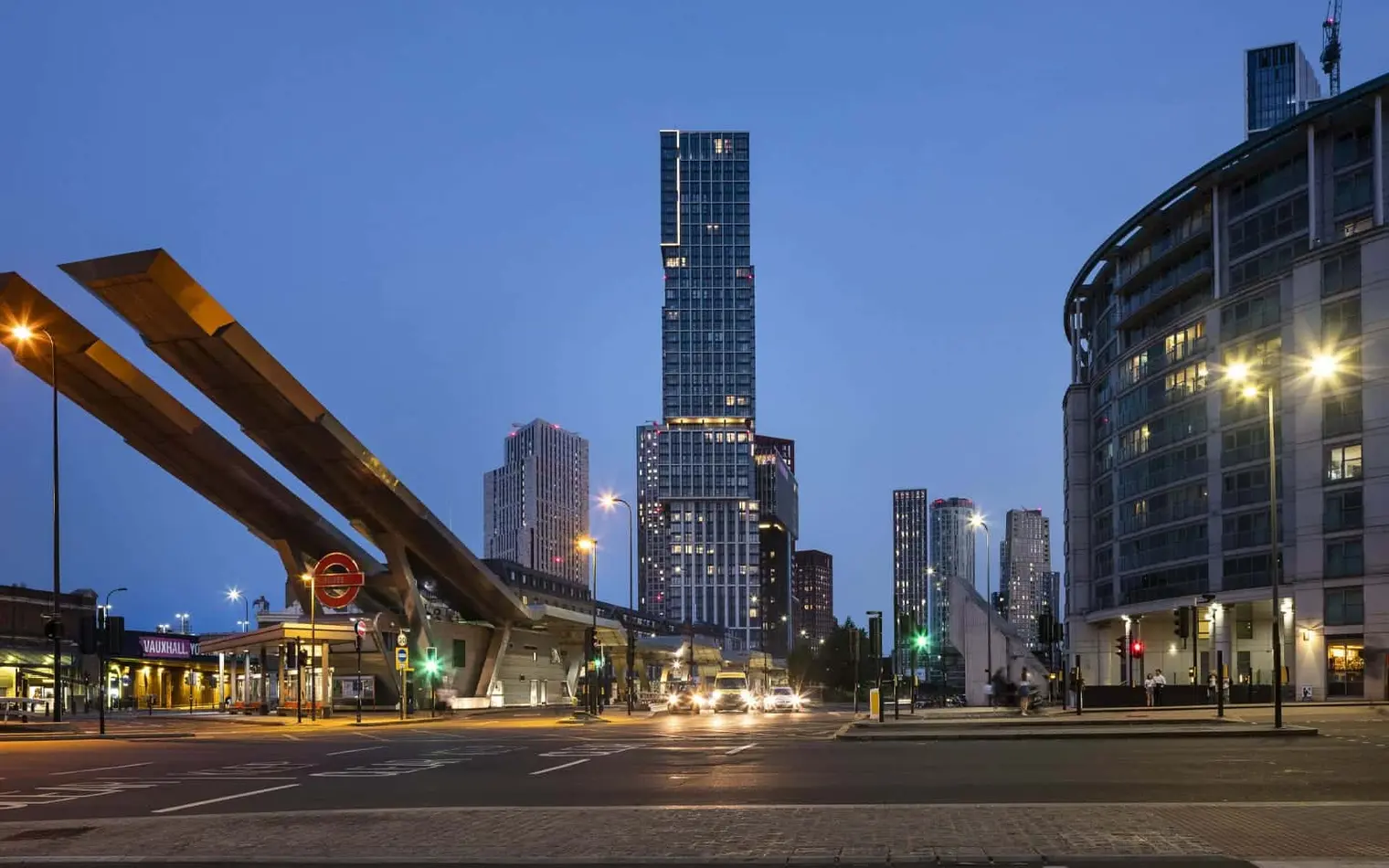 A city street at night with tall buildings in the background.