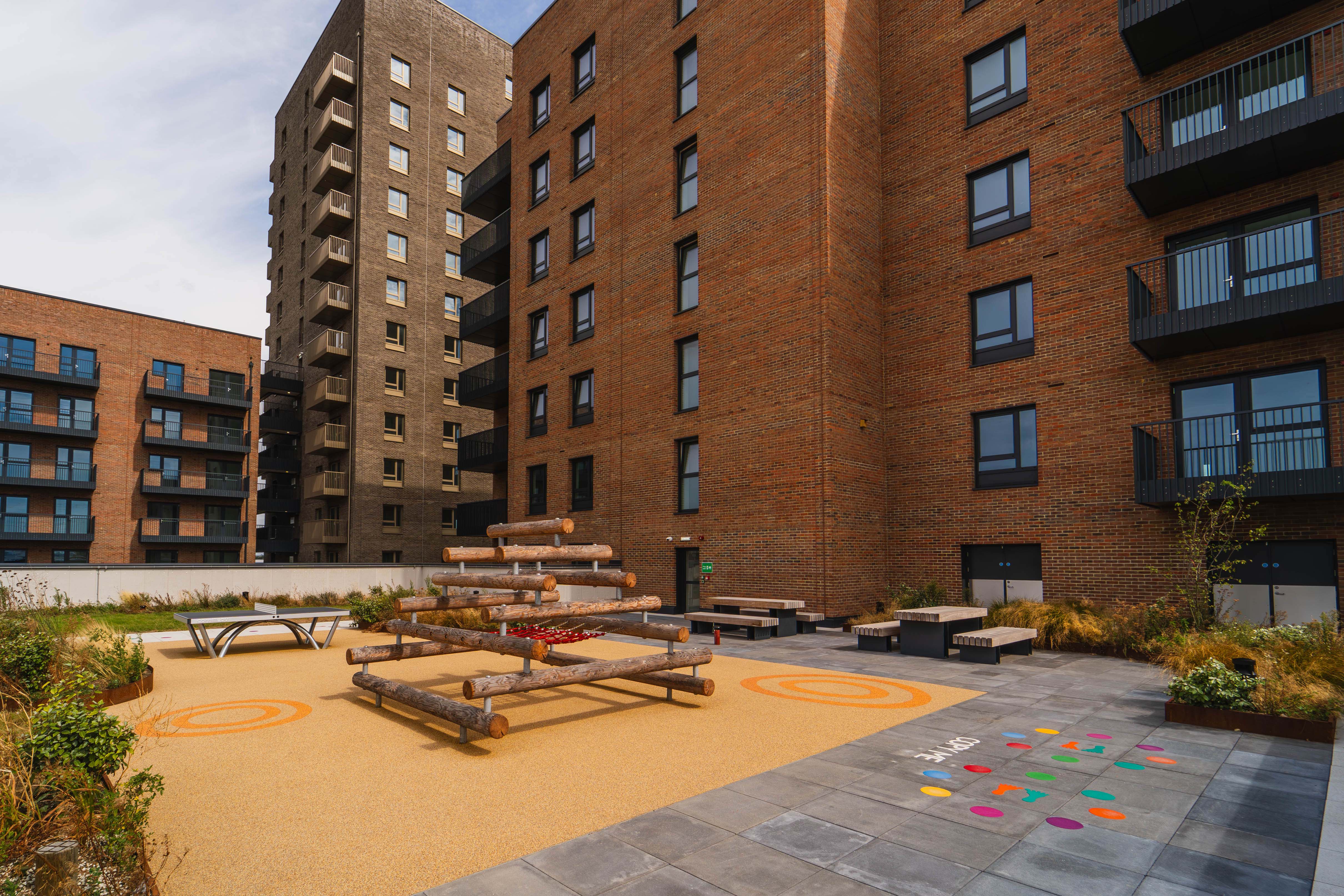 A courtyard with benches and tables in front of a brick building.