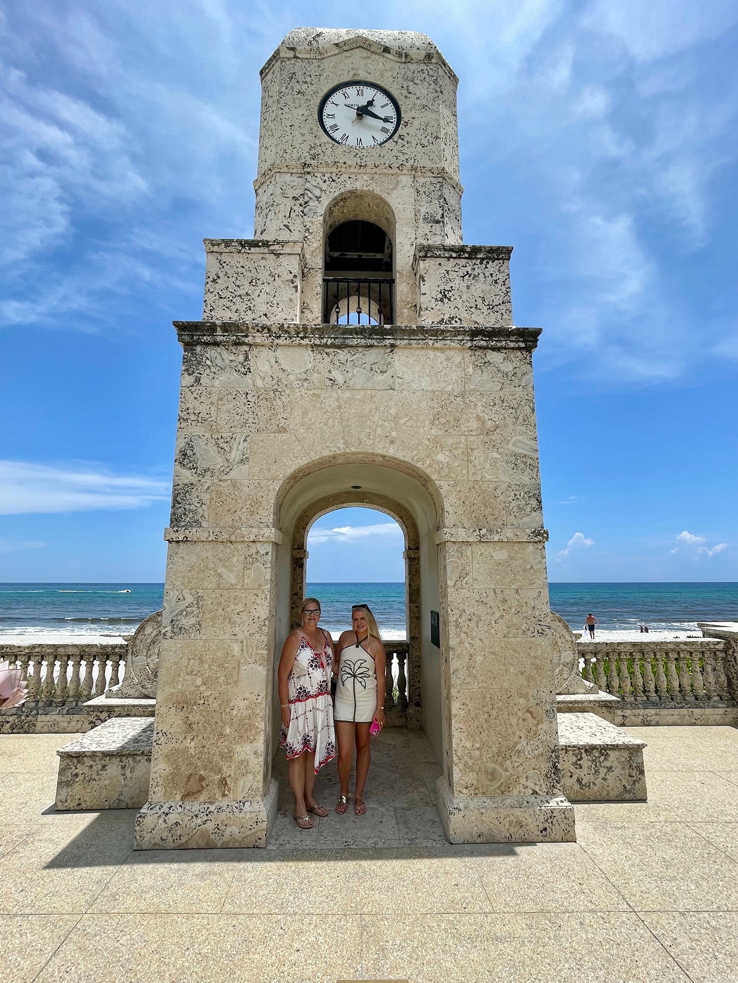 Travelers standing beneath the Palm Beach Clock Tower overlooking the Atlantic Ocean.