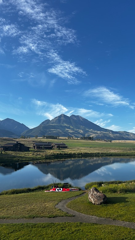 Scenic view of a luxury ranch in Paradise Valley, Montana, with a peaceful lake and surrounding mountain peaks.