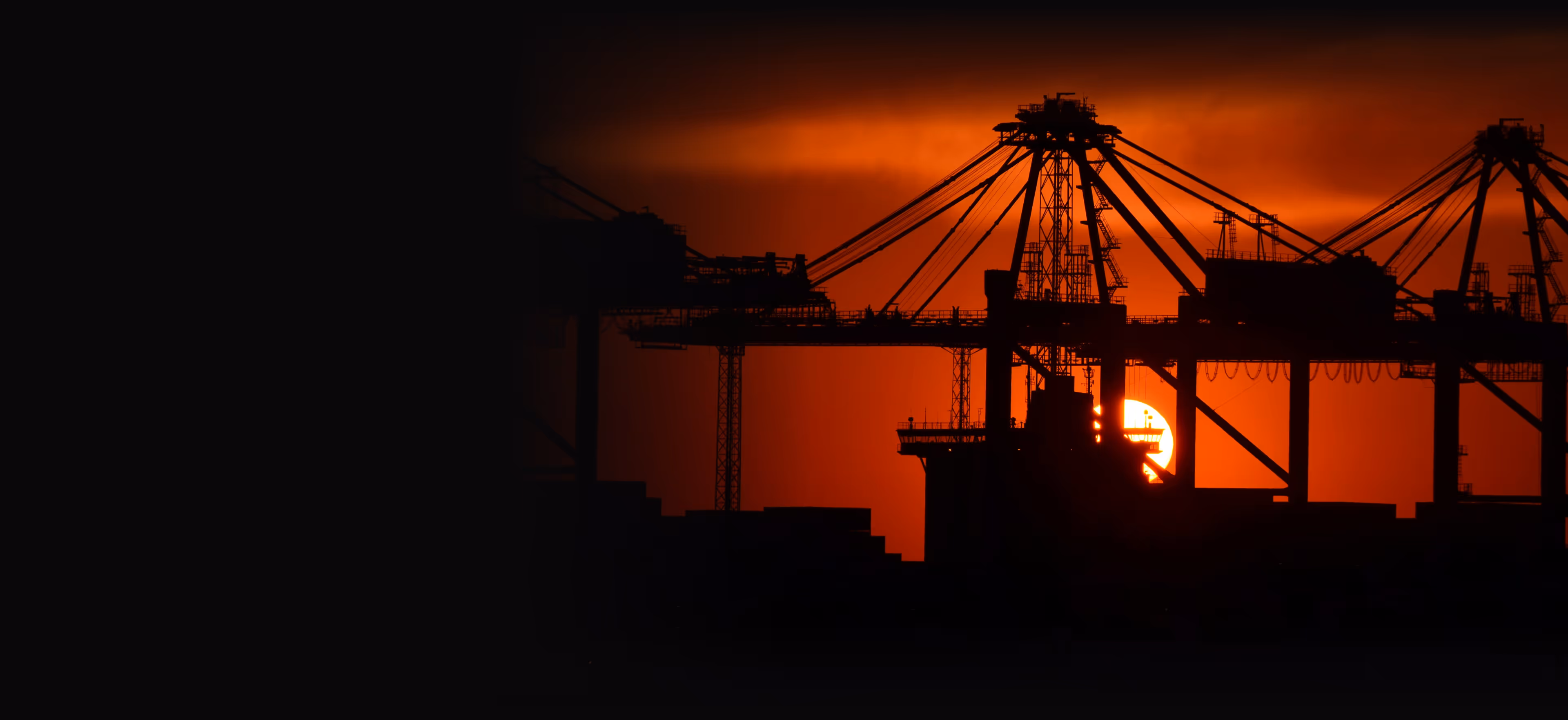 The sun is setting behind a large crane.