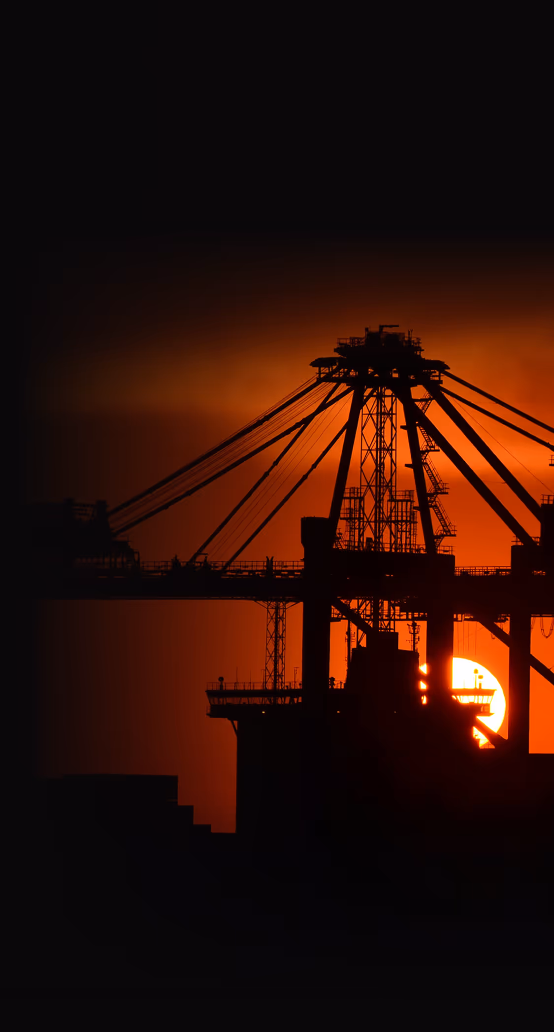 The sun is setting behind a large bridge.
