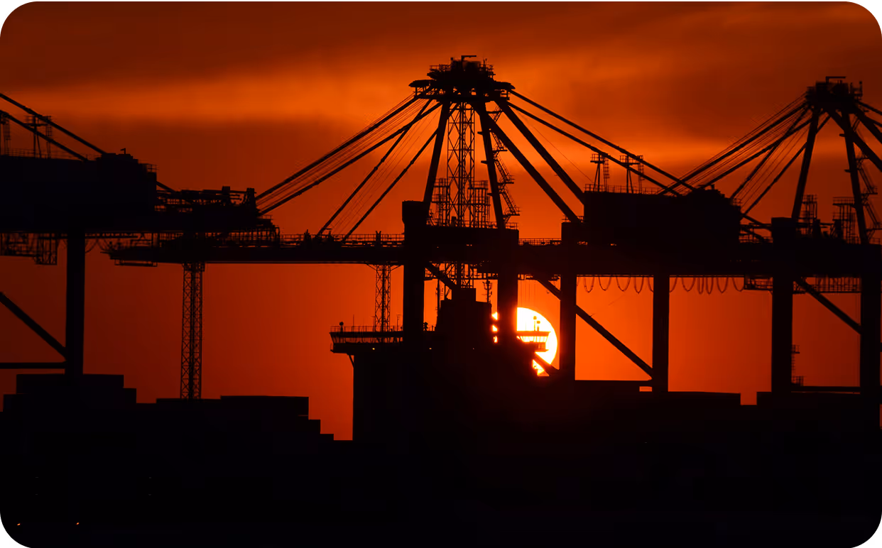 The sun is setting behind a large crane.