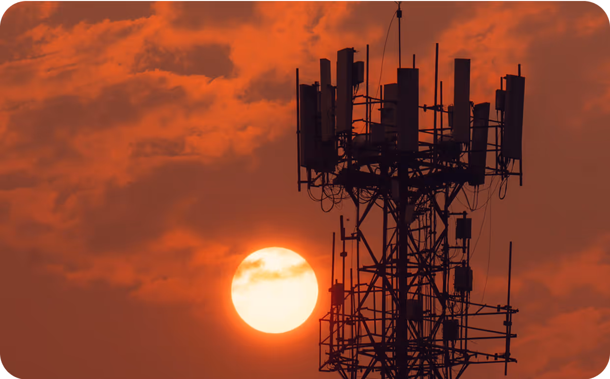 The sun is setting behind a cell tower.