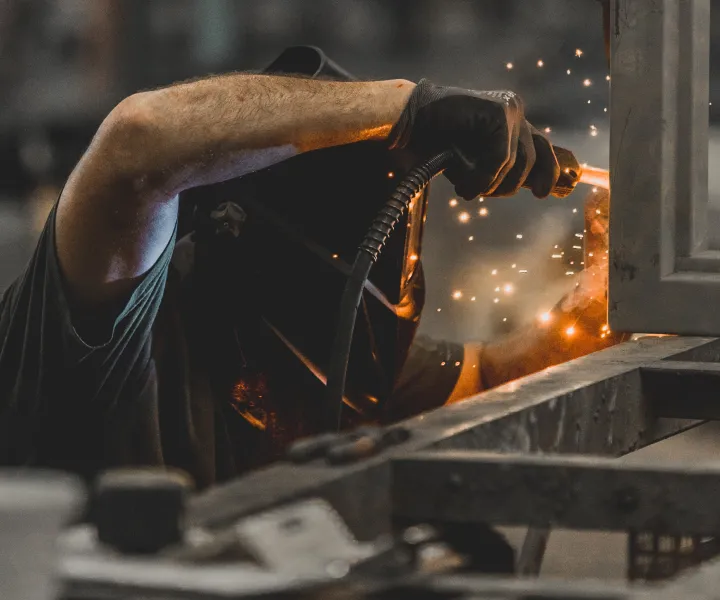 Welder with arm over metal performing a weld