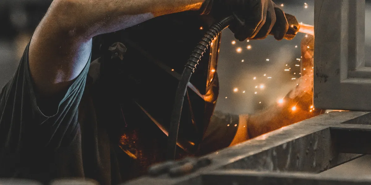Welder with arm over metal performing a weld