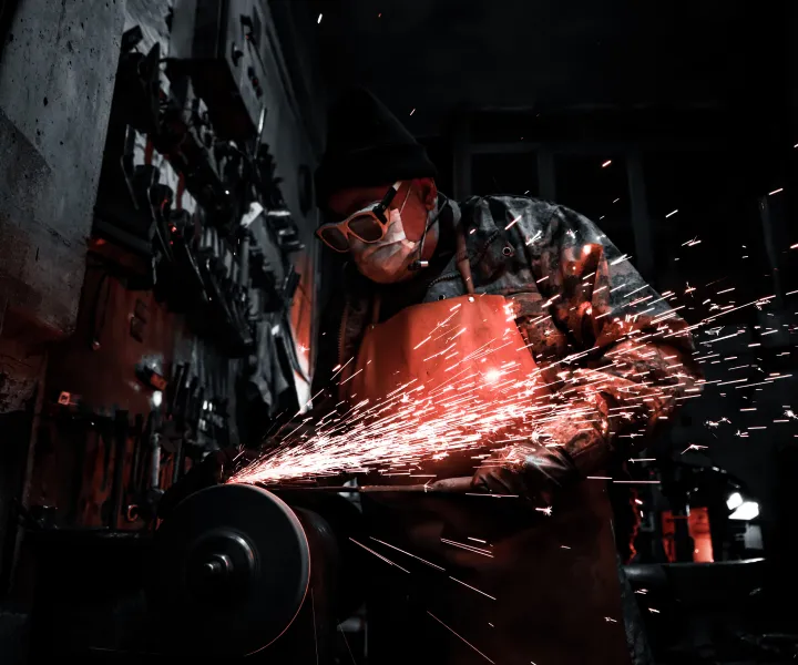 Welder in dark room grinding with red sparks