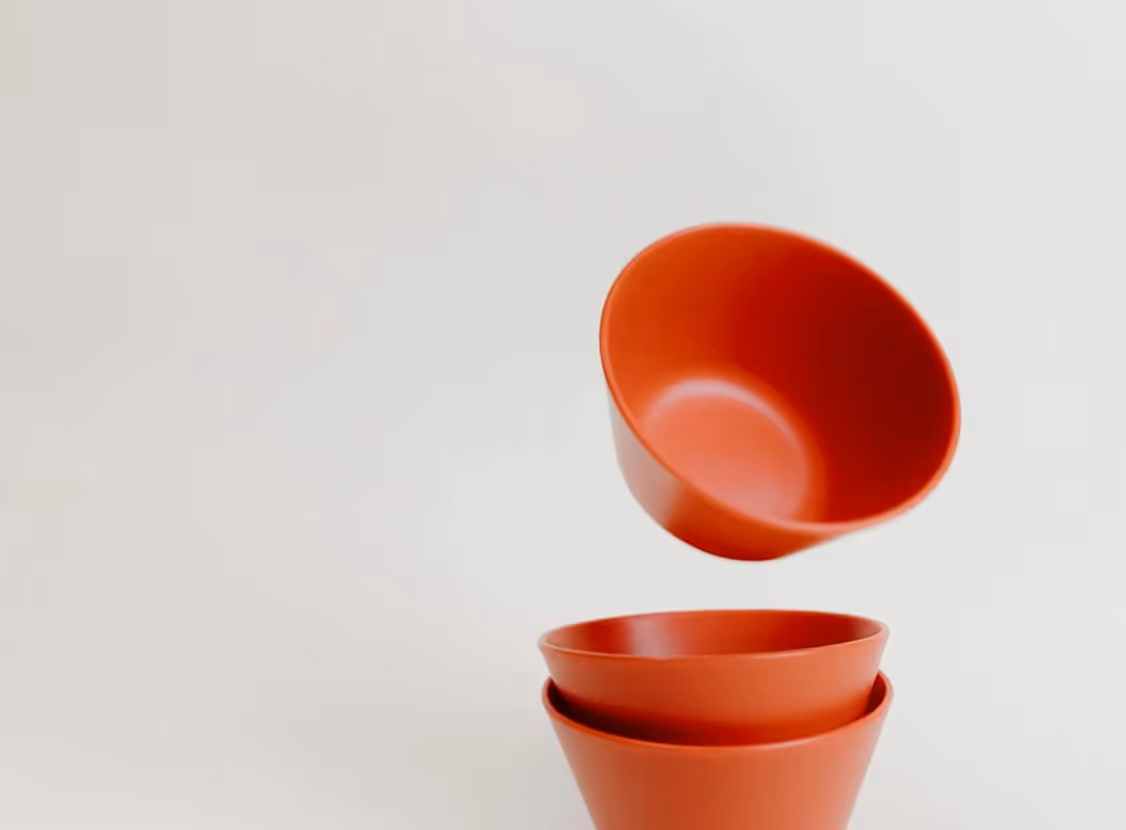 Three stacked red ceramic bowls with one bowl floating above them on a light background.