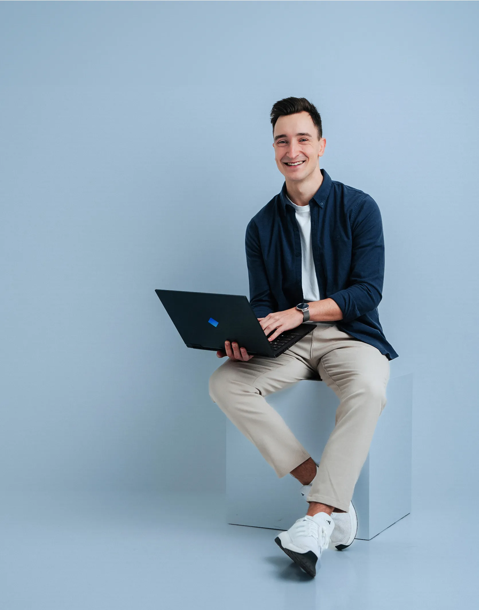 Dominik Walder sitzt mit seinem Laptop in der Hand vor einer Leinwand und lächelt