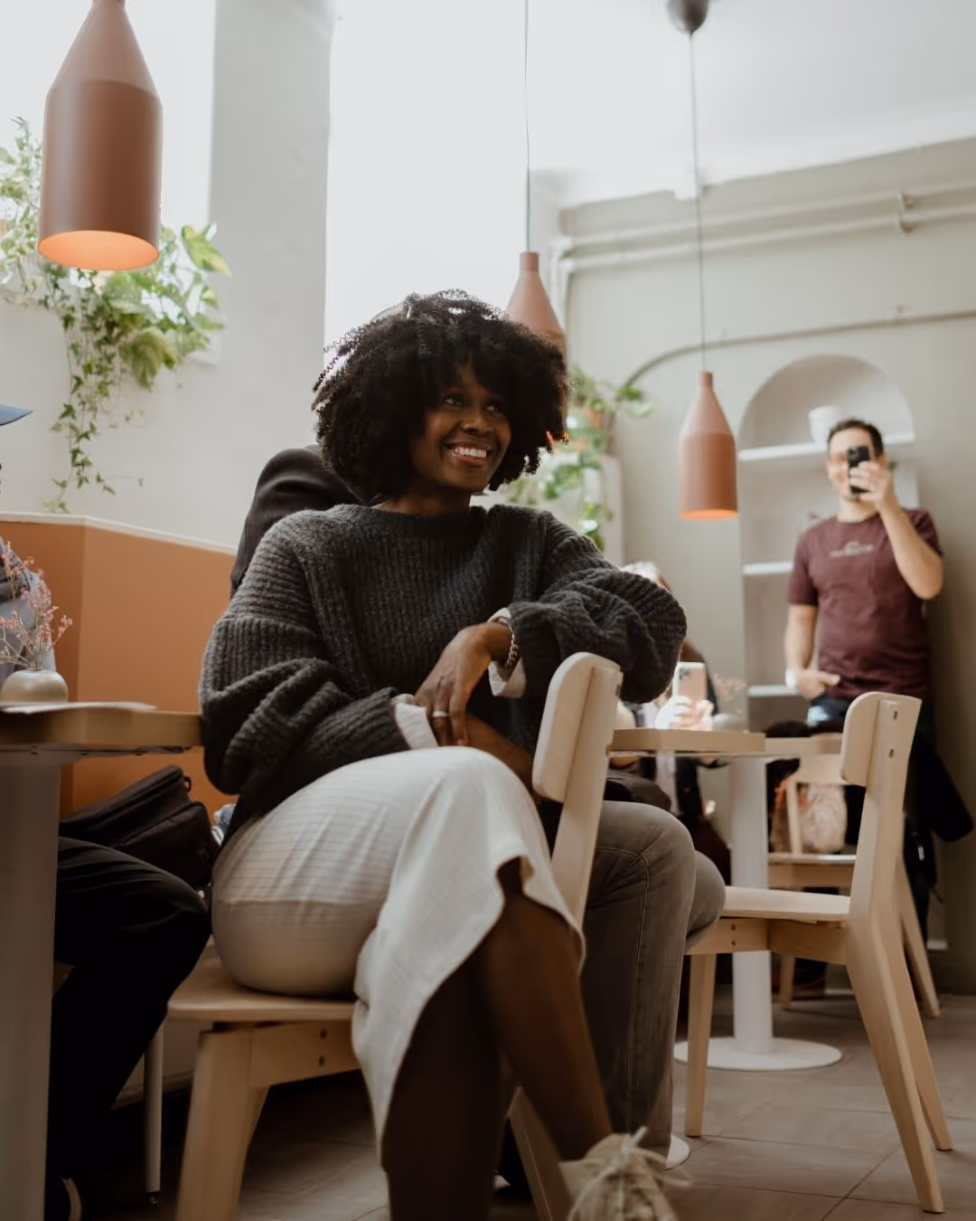 Woman in a brown sweater interacting with a bearded man across a glass display case with baked goods.