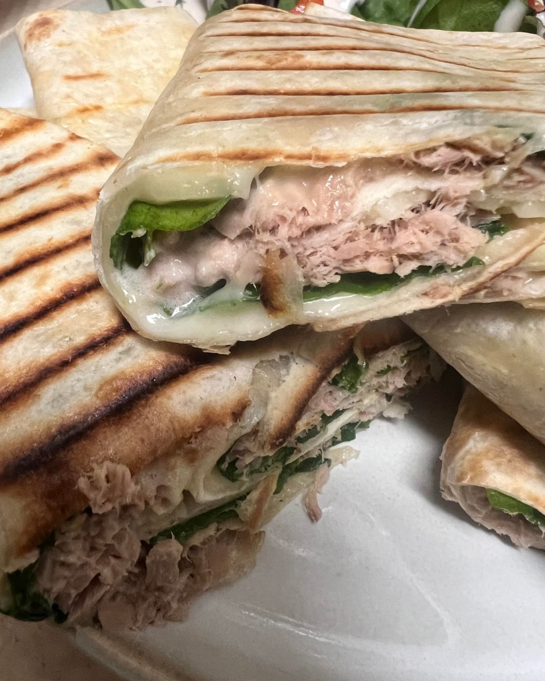 Grilled tuna wraps filled with tuna, leafy greens, and creamy sauce on a plate.