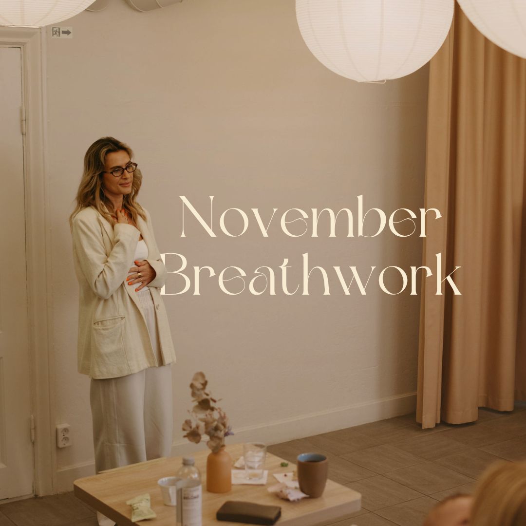 Woman in light-colored outfit standing in a softly lit room with the words 'November Breathwork' on the wall.