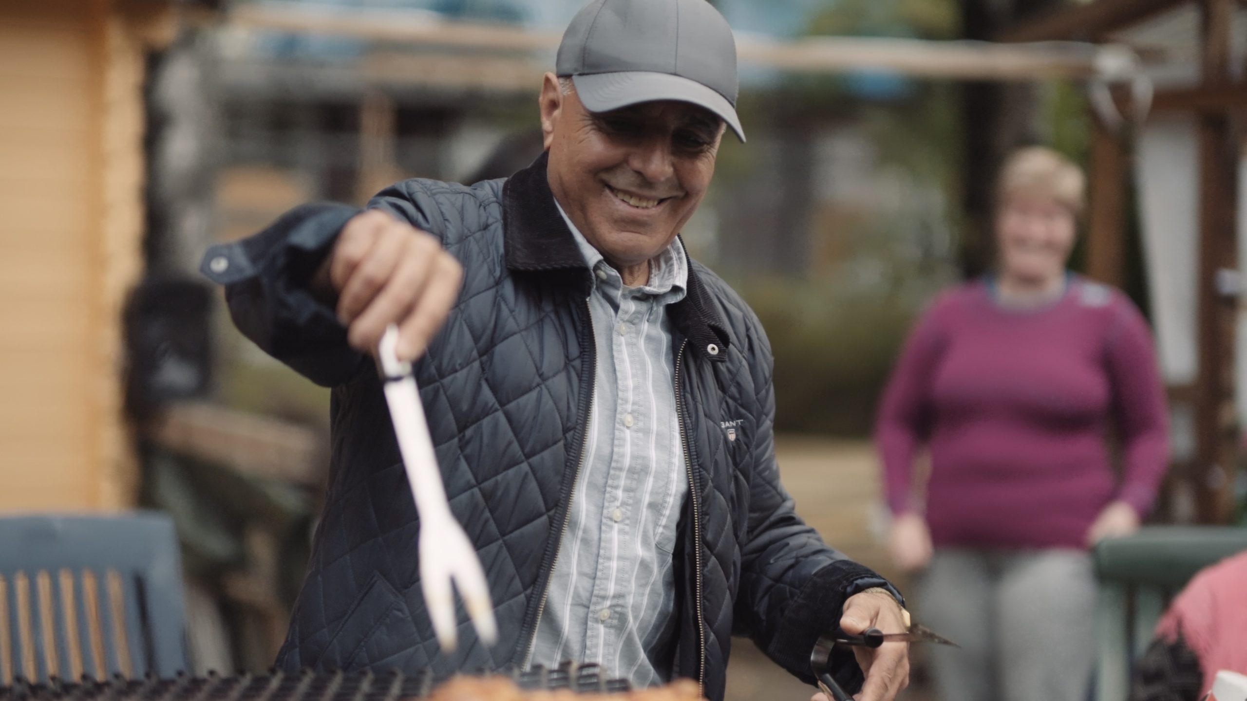 Mann som smiler mens han griller mat på grillen.