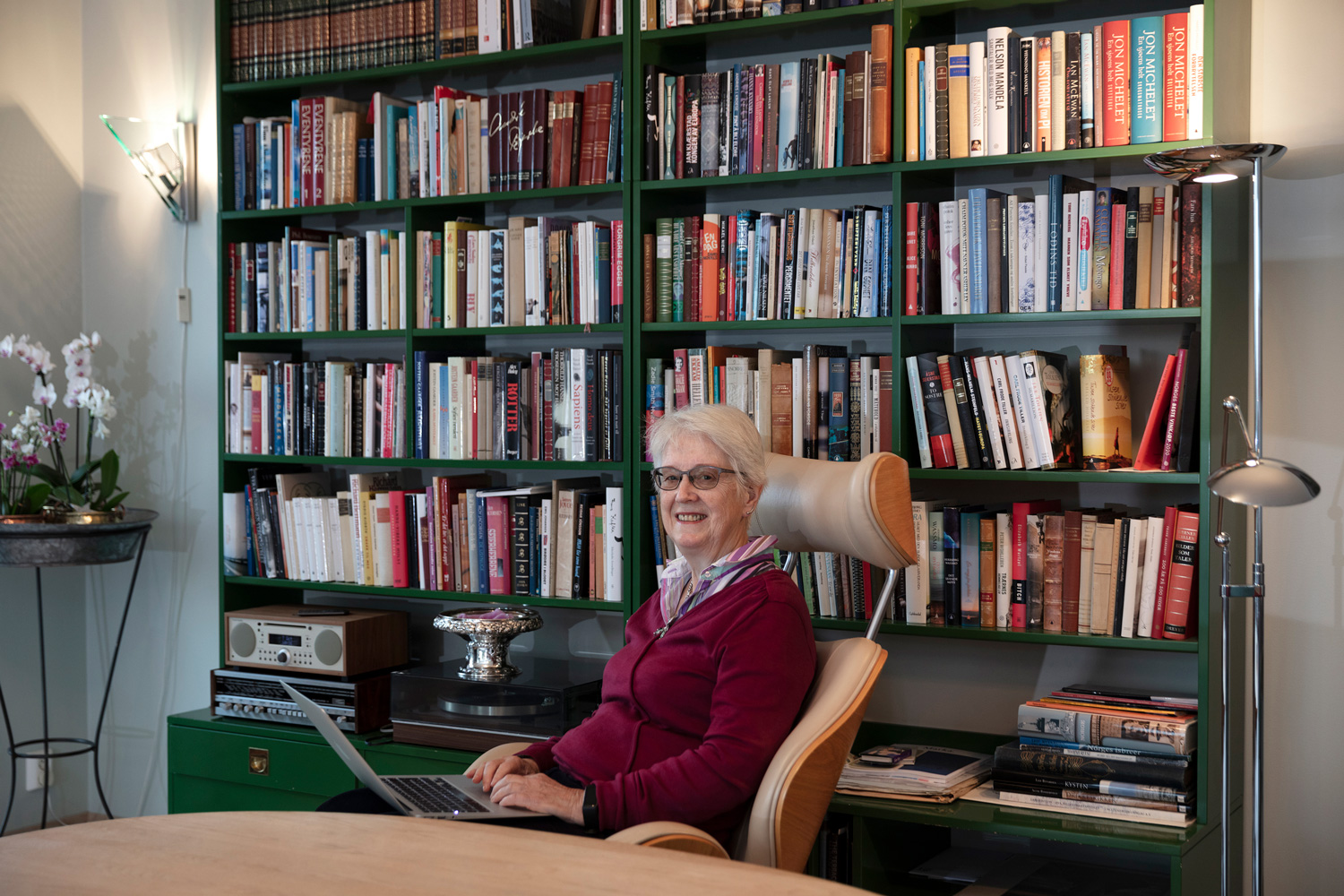 Eldre kvinne som smiler til kamera mens hun er på en laptop.