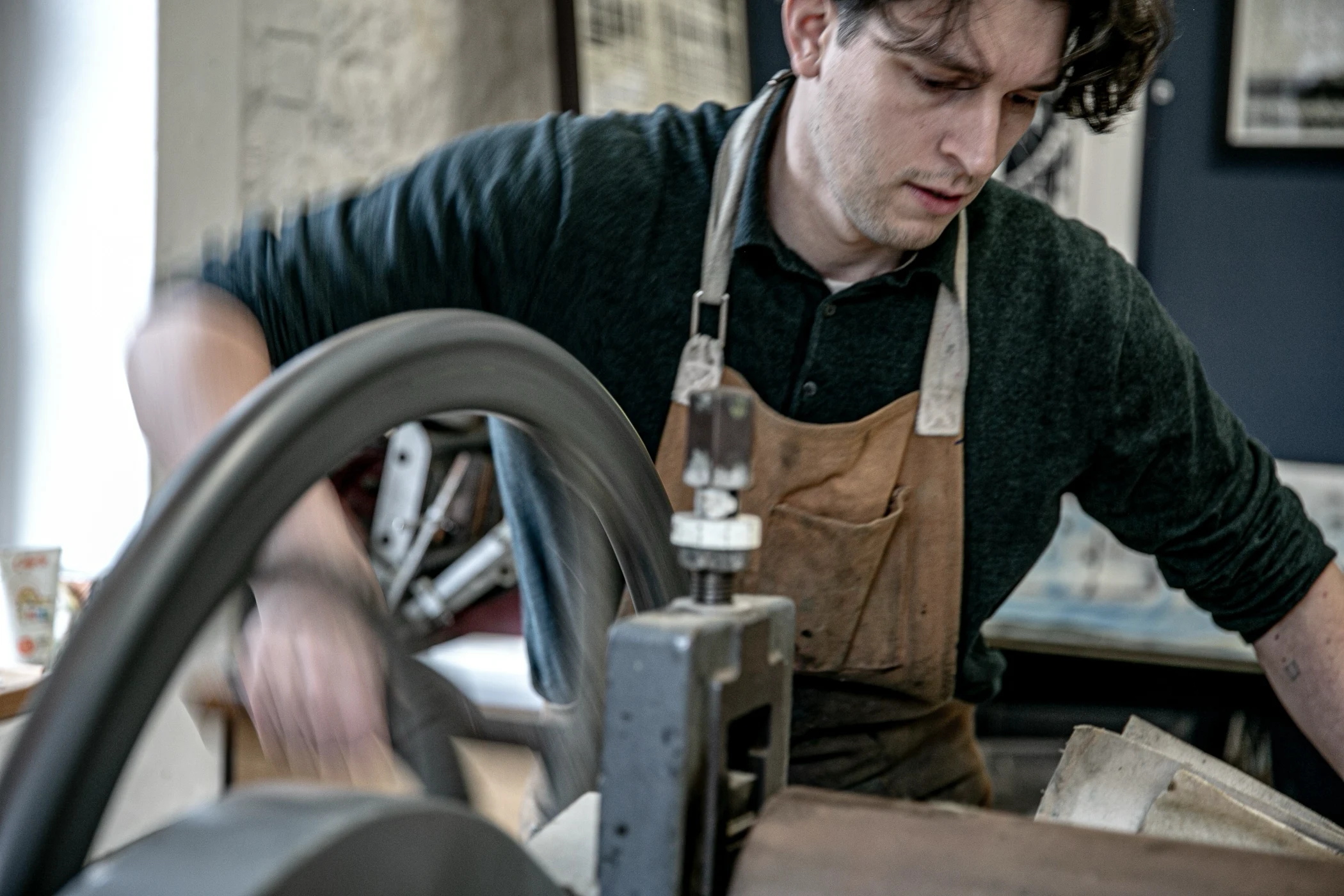 Young man wearing an apron operating a spinning wheel or lathe in a workshop.