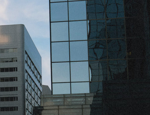 Reflection of adjacent buildings on the glass facade of a modern skyscraper at dusk.