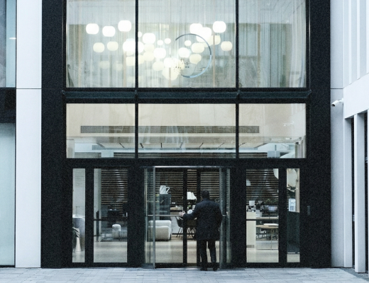 Person standing outside a modern glass entrance door to a building during daytime.