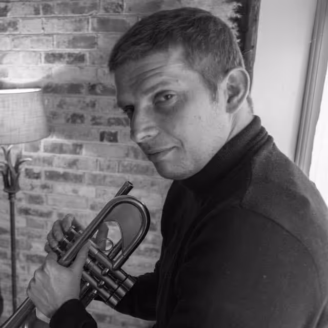 A man holding a trumpet in front of a brick wall.