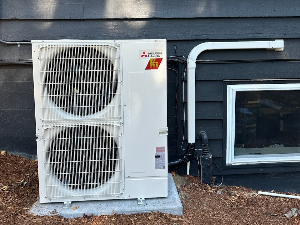 A Mitsubishi heat pump sits next to a blue Tacoma, WA home.