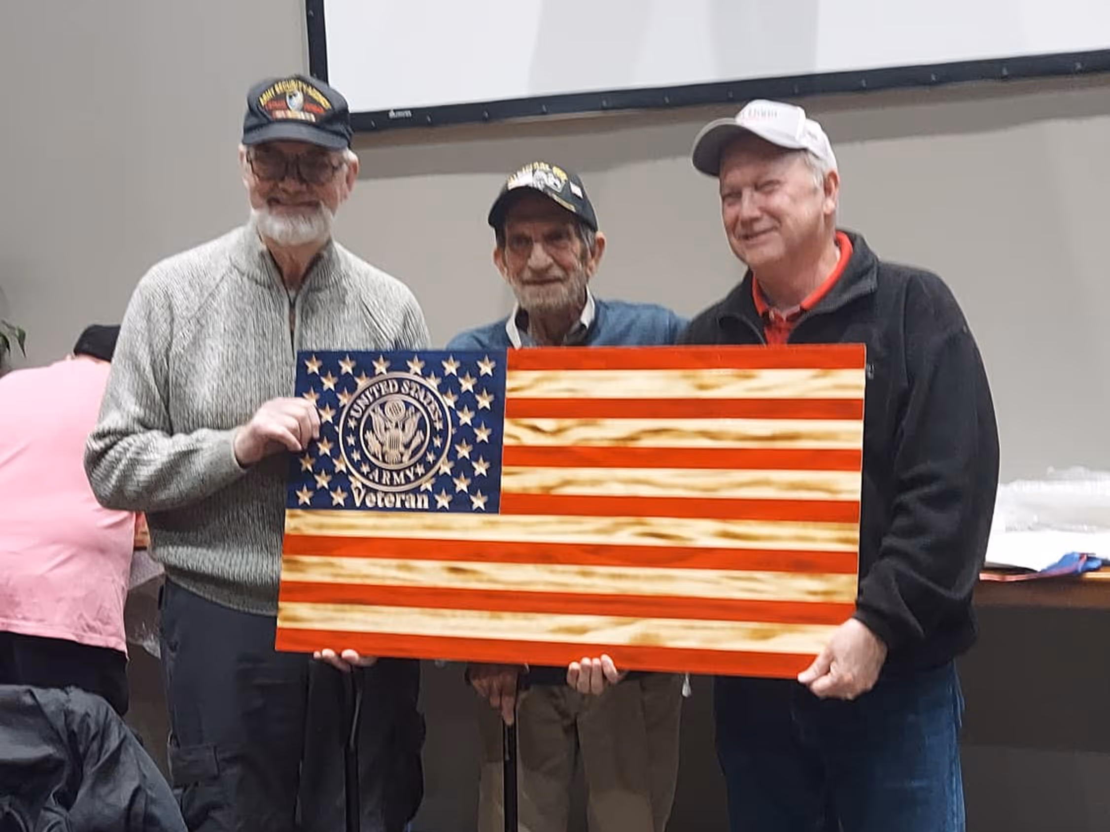 Three veterans holding a wooden U.S. Army veteran flag with stars and red stripes.