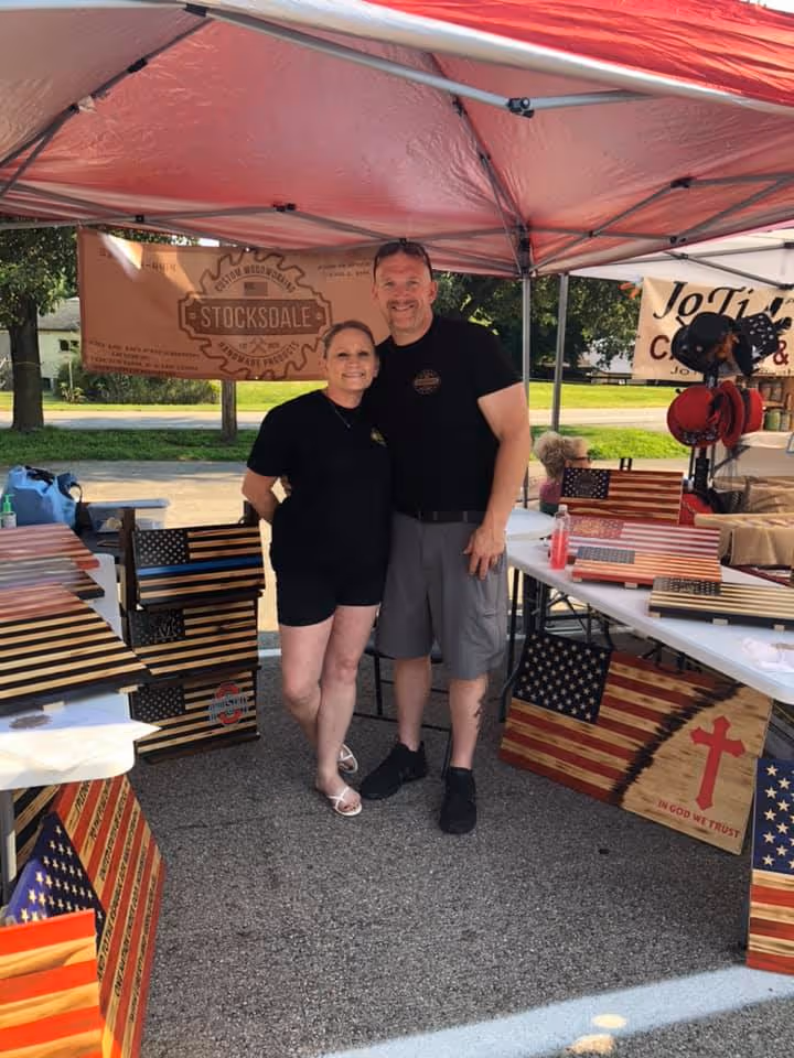 Man and woman standing under a red tent with wooden American flag art displays around them.