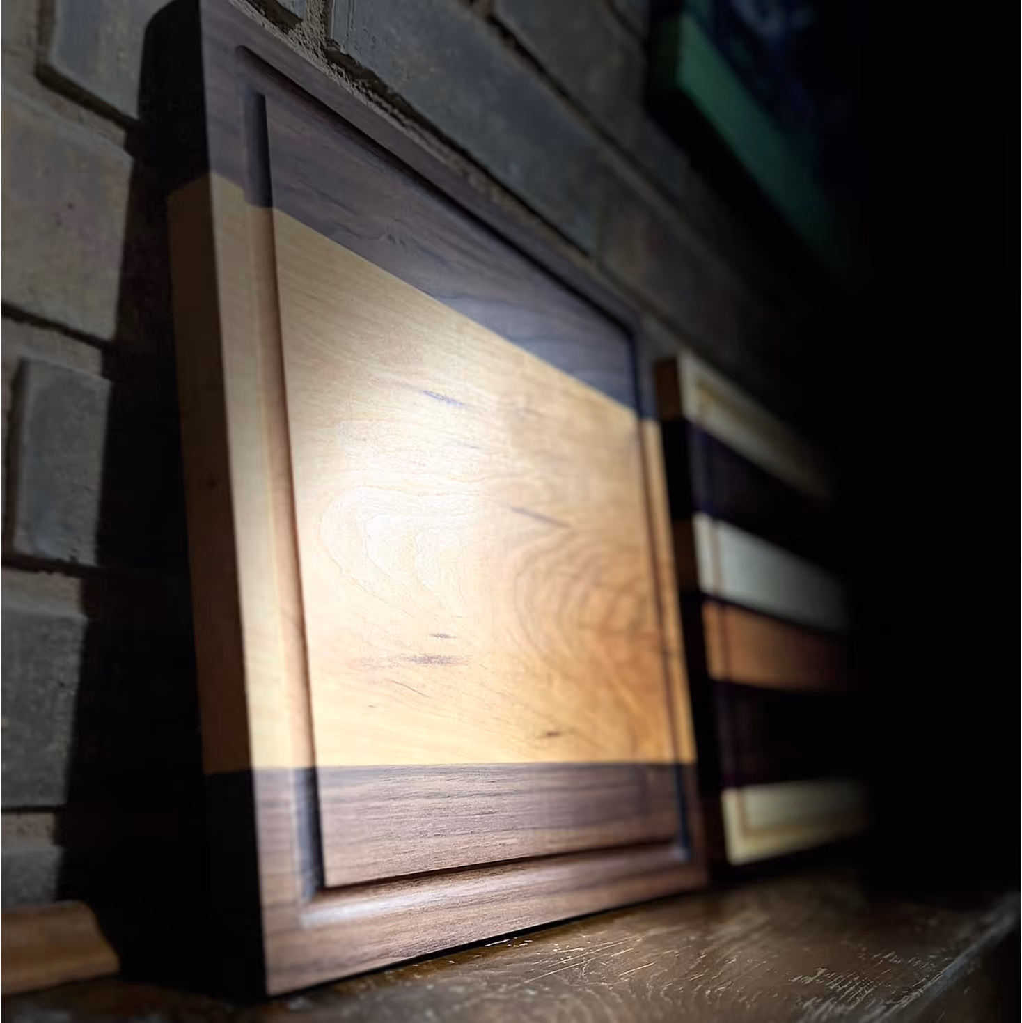 Wooden cutting boards with dark and light wood stripes leaning against a brick wall under light.