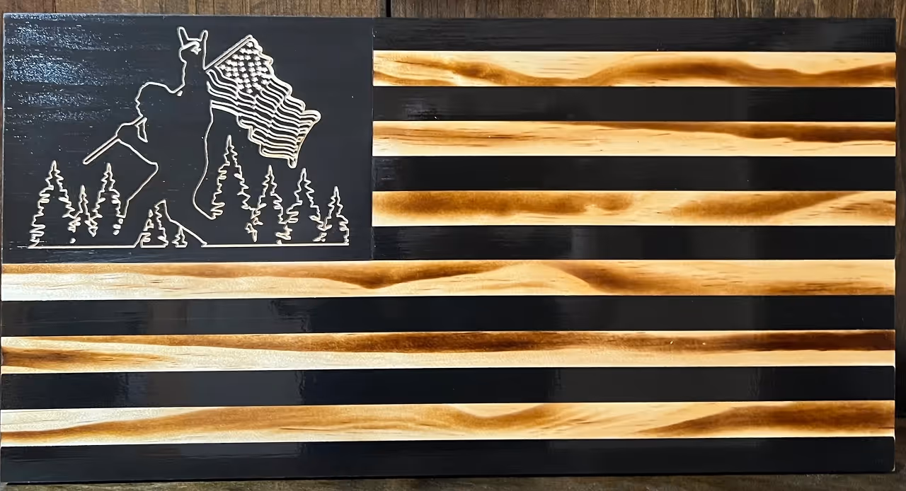Wooden American flag with a carved llama holding the flag among pine trees in the canton area.