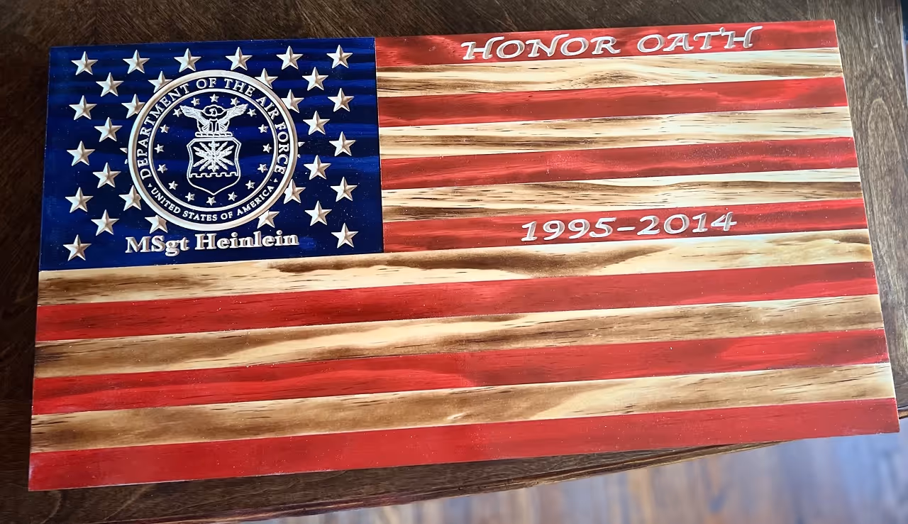 Wooden American flag plaque with Air Force emblem, name MSGT Heinlein, and dates 1995-2014.