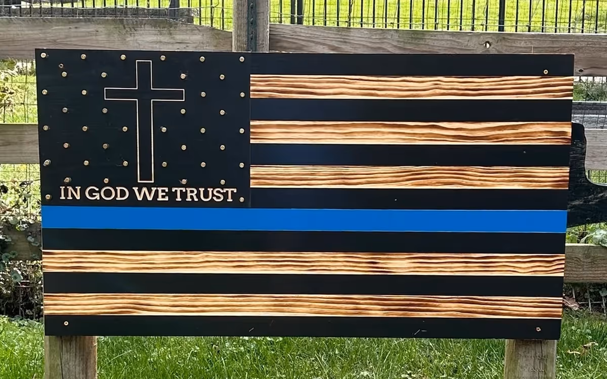 Wooden American flag with a cross, stars, 'IN GOD WE TRUST' and a blue stripe.