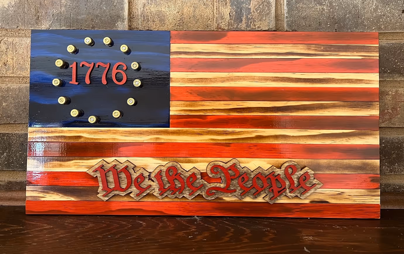 Wooden American flag with '1776' surrounded by bullet casings and 'We the People' in red lettering.