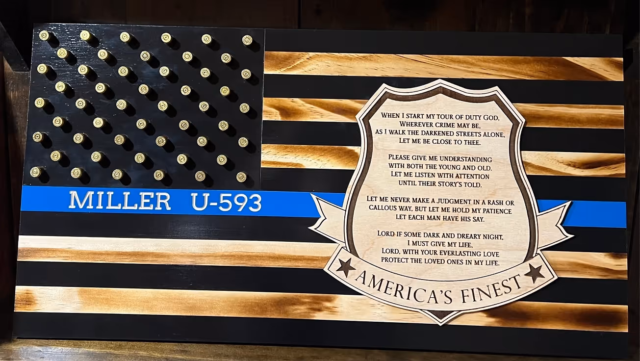 Wooden American flag with bullet heads as stars, blue stripe with 'MILLER U-593,' and a police shield poem.