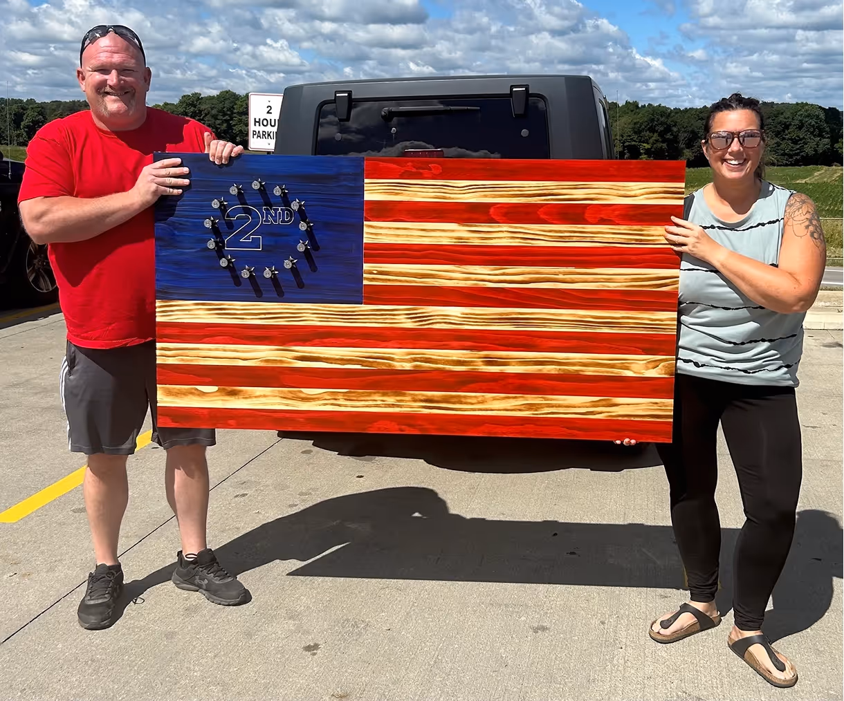 Two people holding a wooden US flag with 2ND inside stars in the blue field.