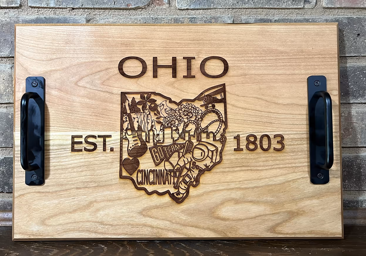 Wooden serving tray engraved with Ohio state outline, symbols, and text EST. 1803 with black handles.