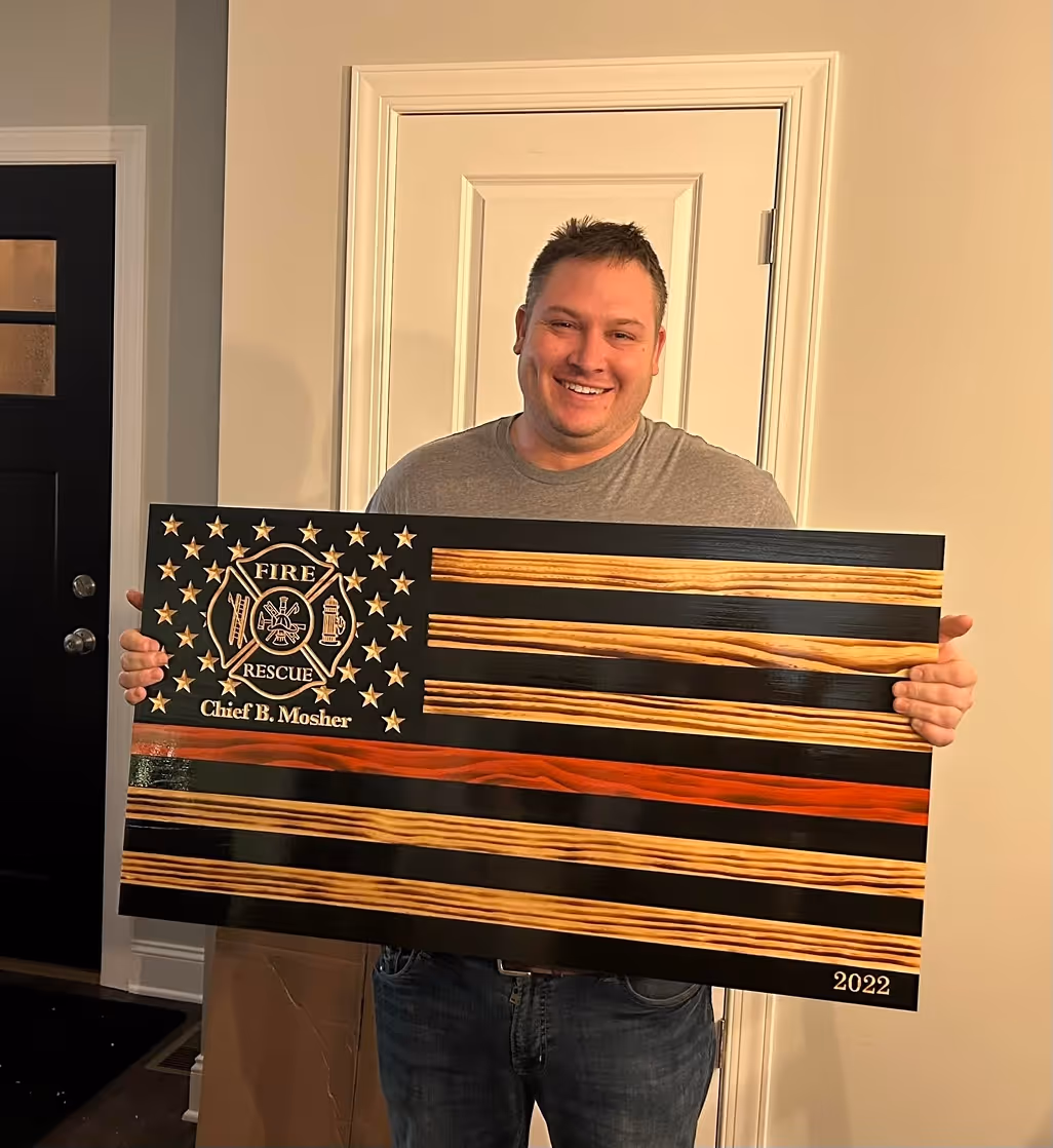 Smiling man holding a wooden Fire Rescue flag plaque with a red stripe and Chief B. Mosher engraved.