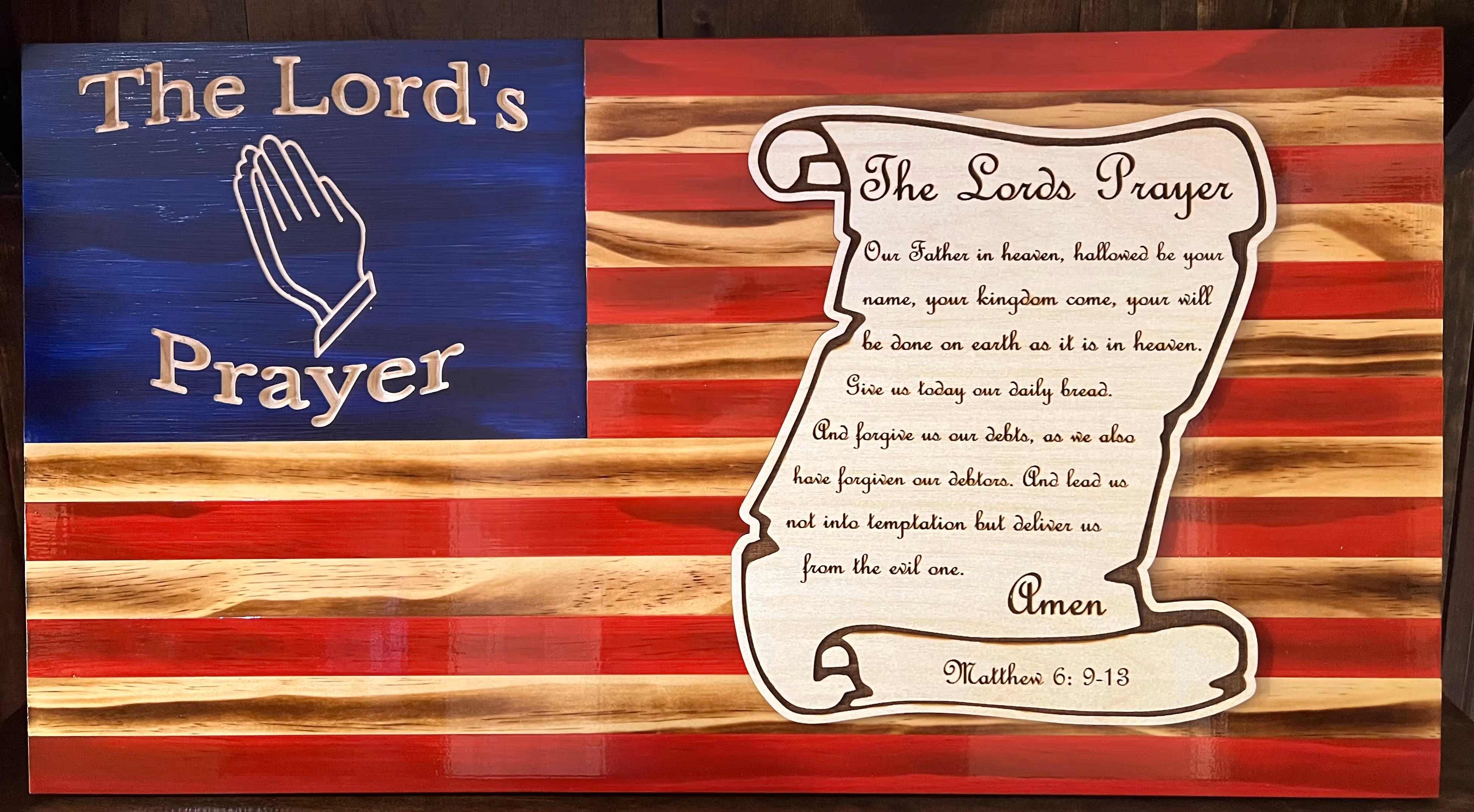Wooden American flag with The Lord's Prayer text and praying hands symbol carved in blue field.