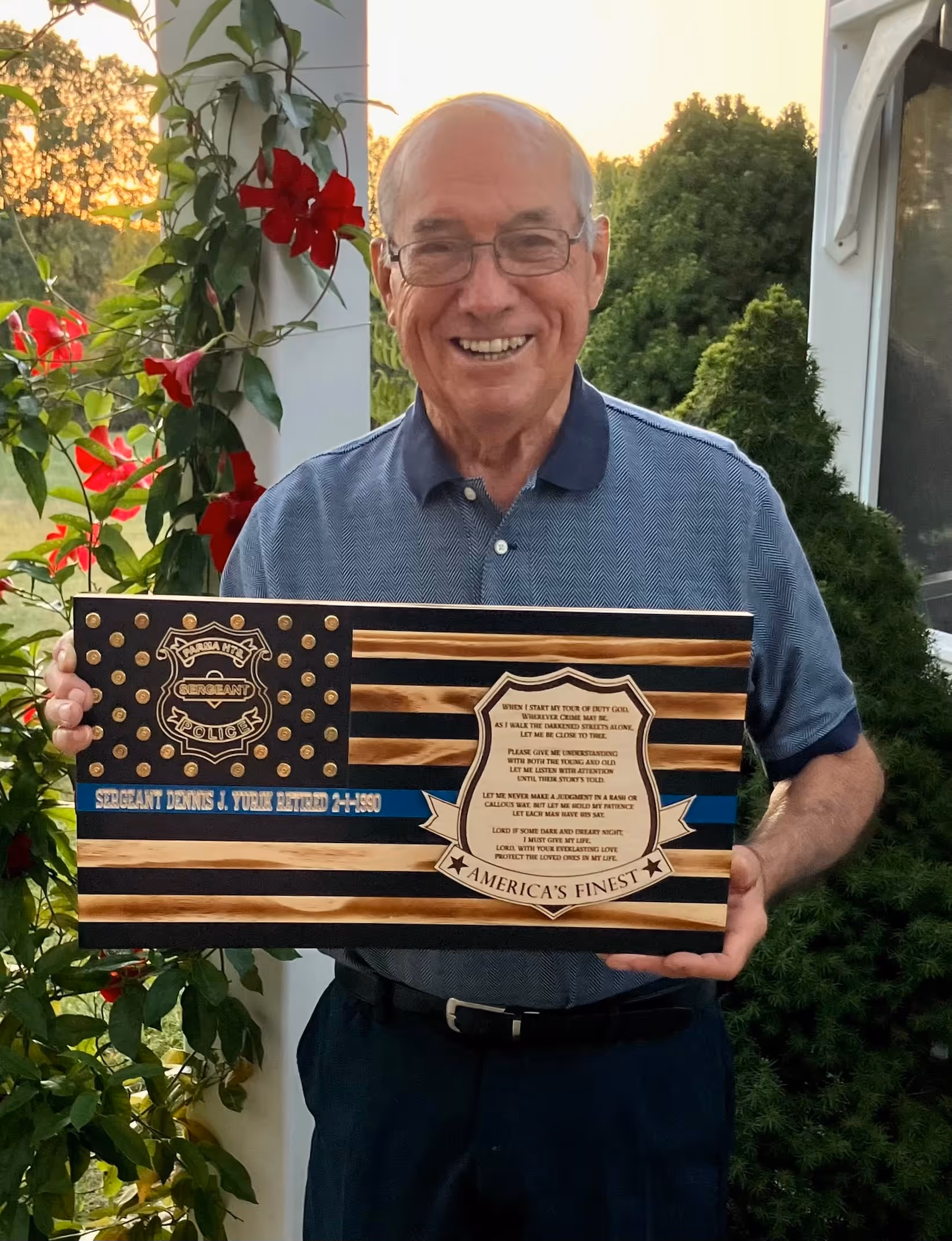 Smiling elderly man holding wooden plaque with police badge and American flag design.