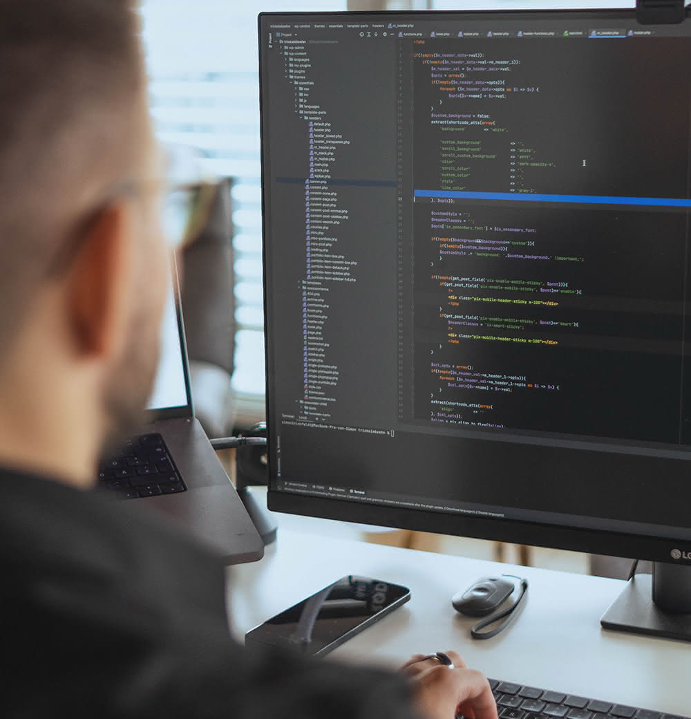 Person sitzt vor zwei Bildschirmen, auf einem ist Programmiercode sichtbar.