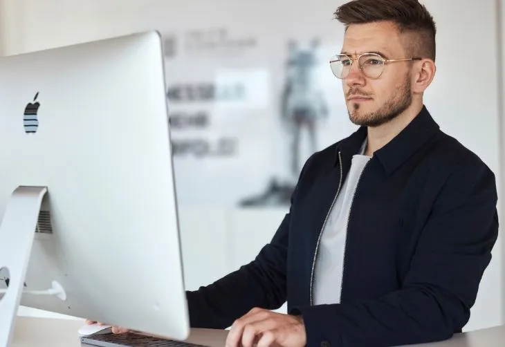 Mann mit Brille sitzt konzentriert vor einem Apple-Computer und arbeitet.