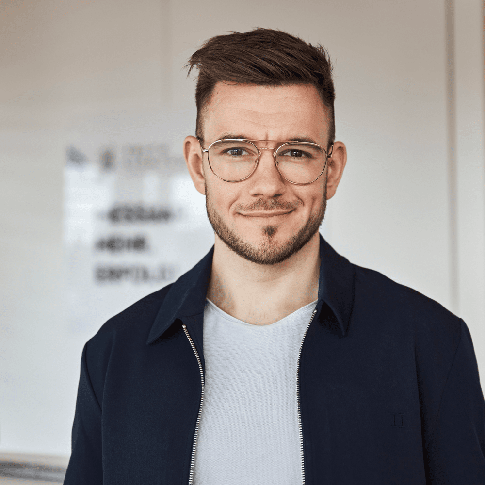 Lächelnder Mann mit kurzem braunem Haar, Brille und dunkelblauer Jacke.