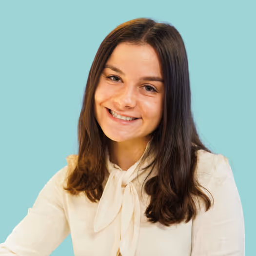 Smiling woman with long brown hair wearing a light blouse against a turquoise background.