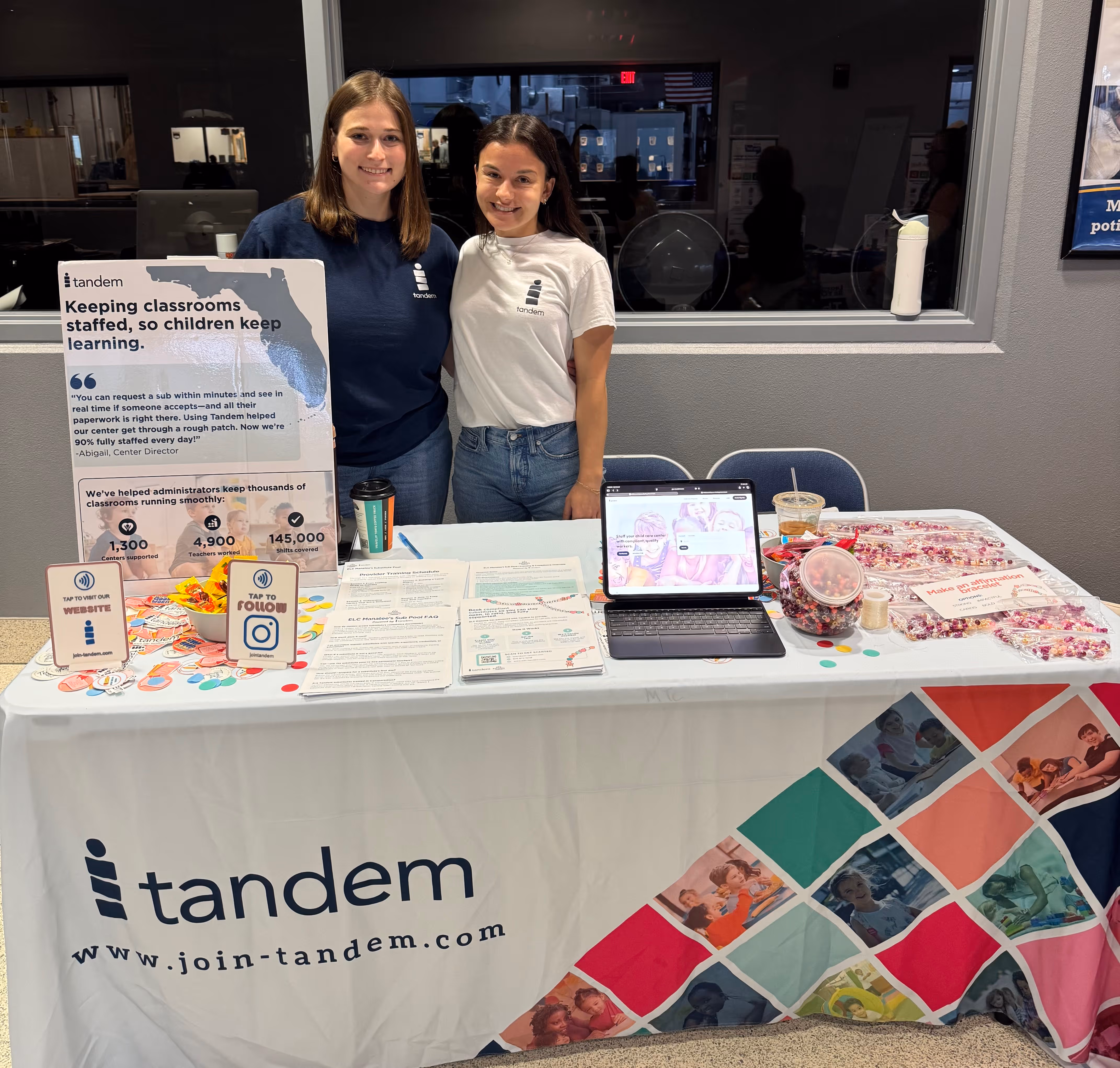 The Tandem founders stand behind a Tandem table with informational materials and a laptop at an indoor event.