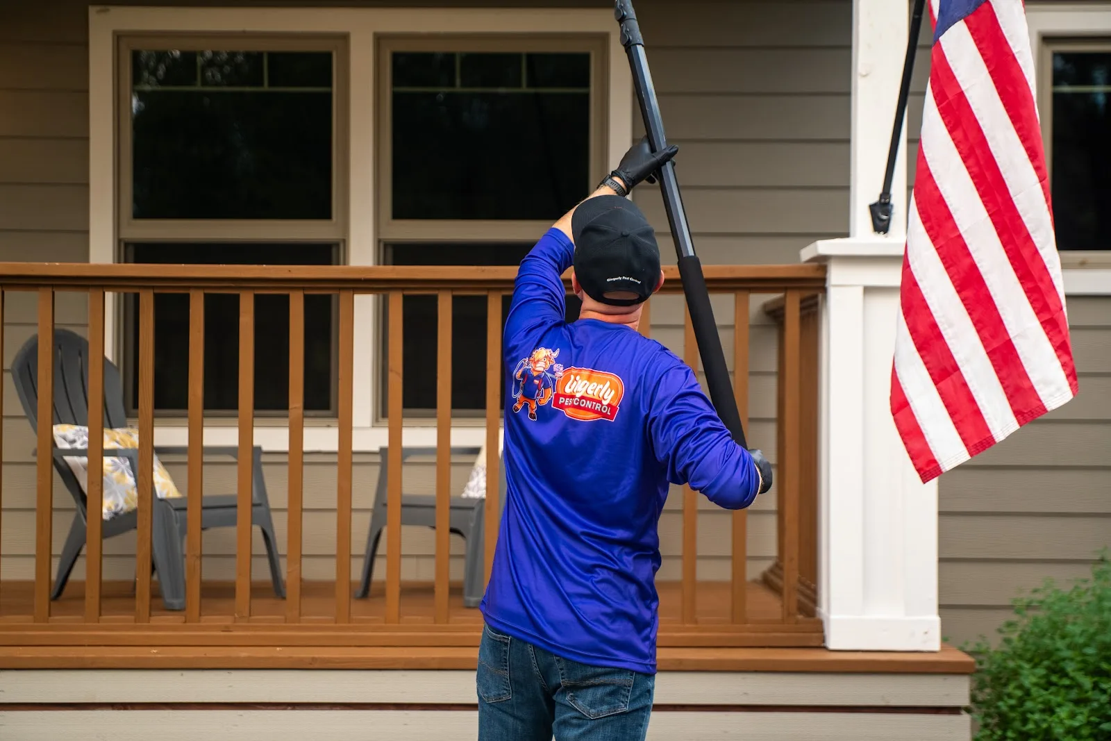 Gingerly Pest Control owner removing spider webs from a porch eave with an extension pole in Lincoln, CA