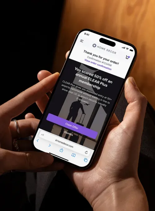 Person holding smartphone displaying a confirmation page from Home Decor with a 50% off offer for an annual CLEAR Plus membership.