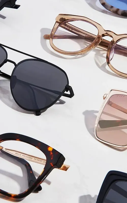 Close-up of various stylish eyeglasses and sunglasses with different frame colors and shapes laid out on a white surface.
