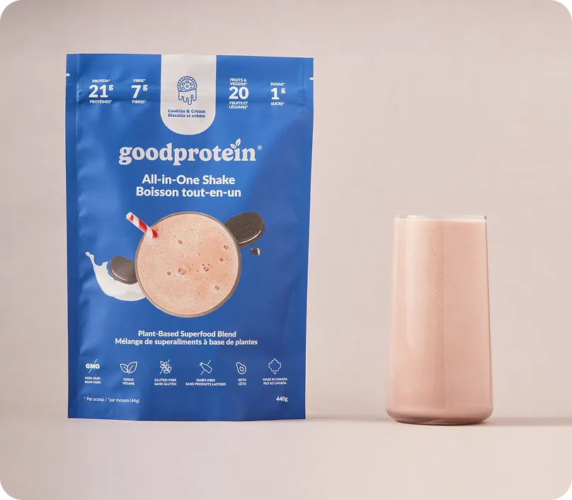 Blue package of goodprotein All-in-One Shake with cookies and cream flavor next to a glass filled with a light brown shake.