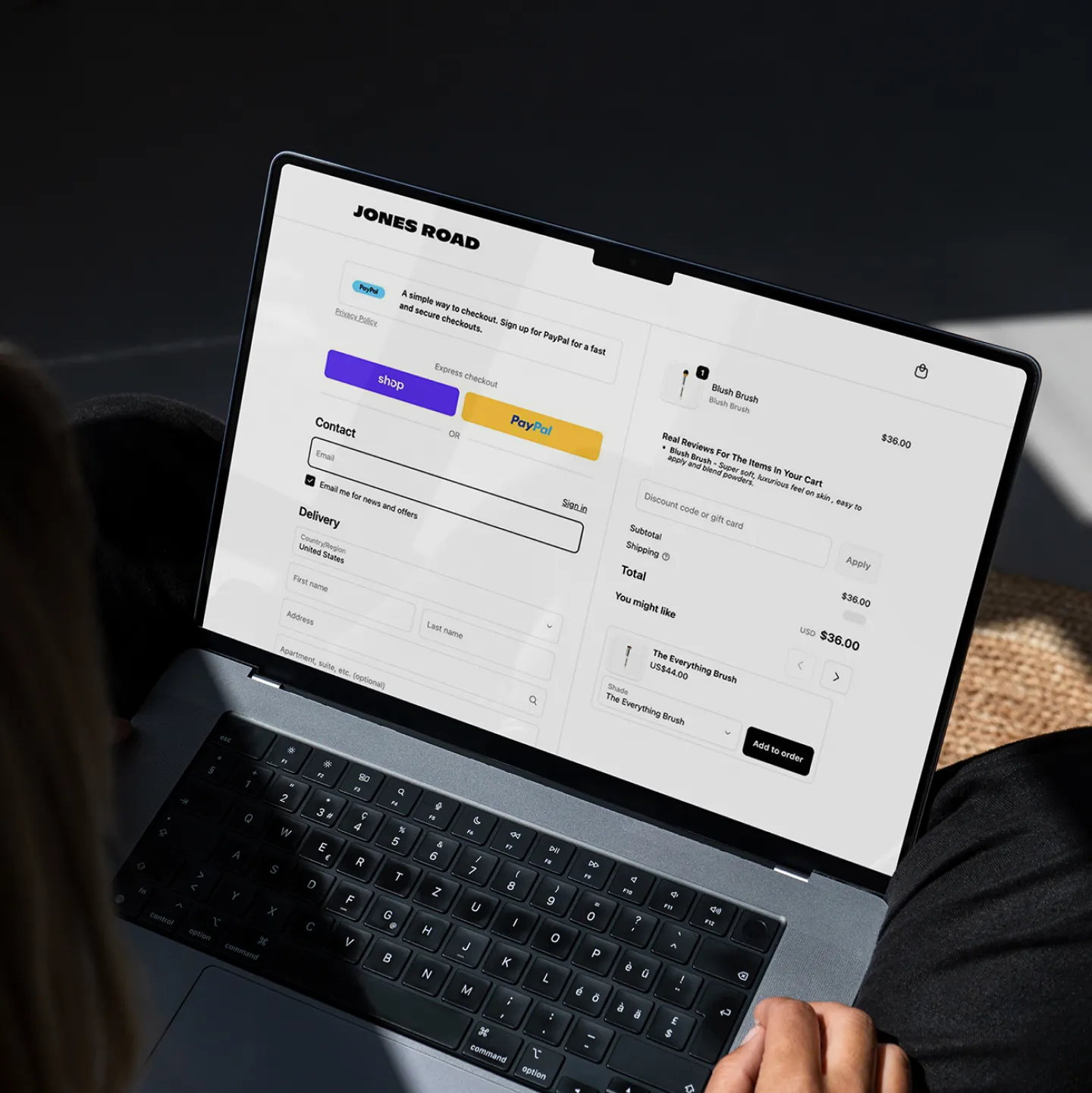 Person using a laptop displaying a Jones Road online checkout page with options to shop, pay with PayPal, and a cart showing a blush brush priced at $36.
