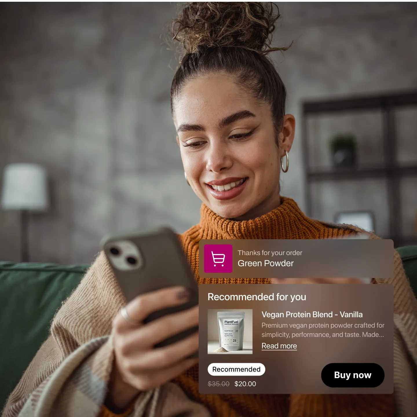 Smiling woman in an orange sweater holding a smartphone with an on-screen order confirmation and product recommendation for vegan protein powder.