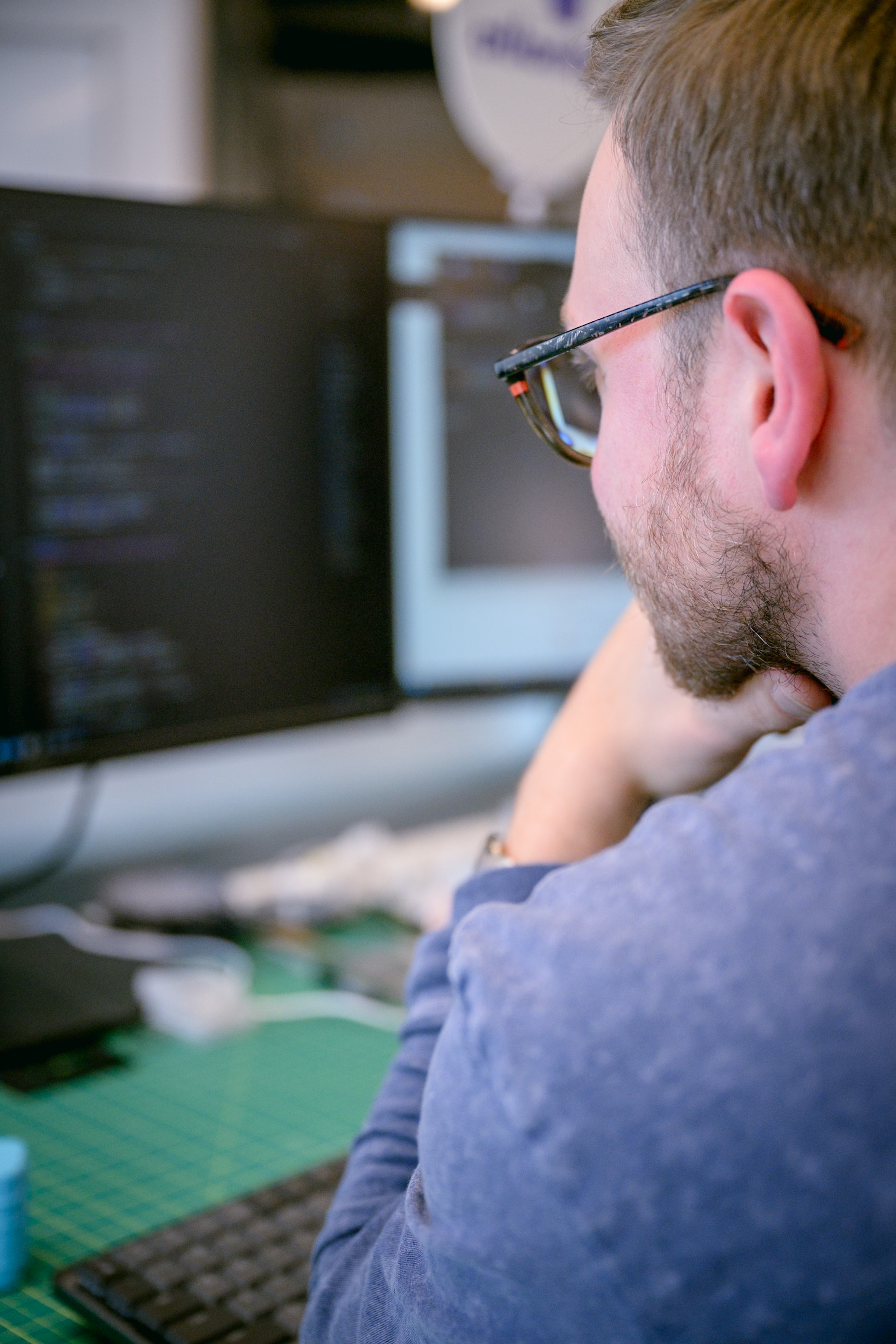 A builder with glasses working at a desk with two monitors.