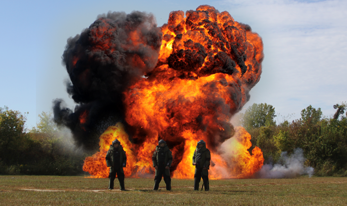 three members of the bomb squad stand in front of a huge billow of fire