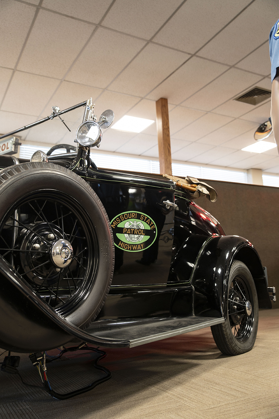 A very old Highway Patrol car from the 1930s era sits on the museum showroom floor.